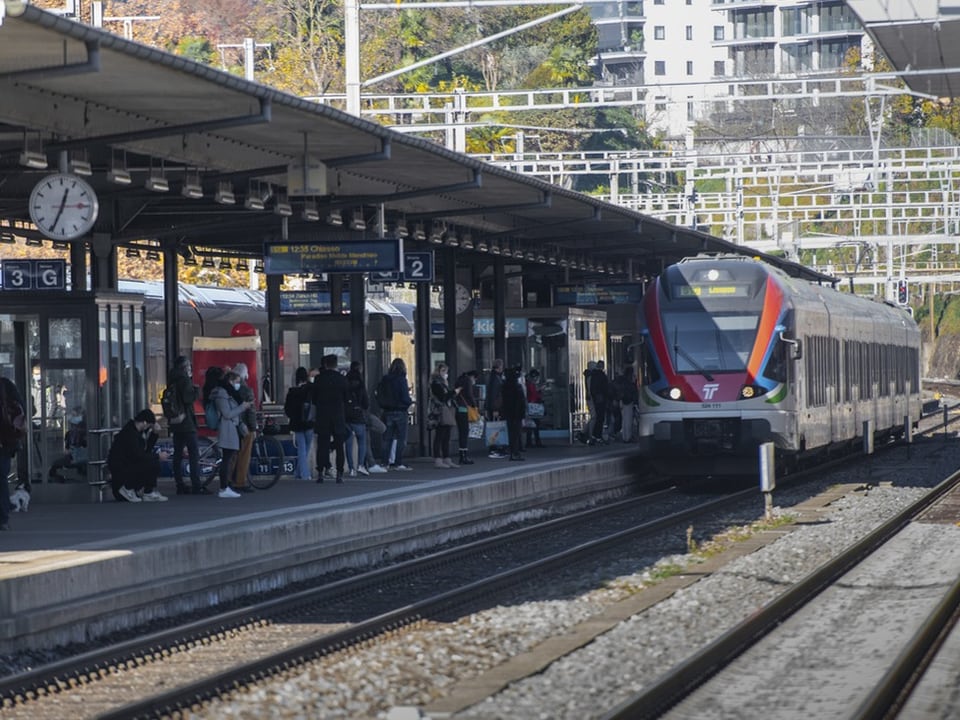 Menschen auf einem Bahnsteig mit einfahrendem Zug.