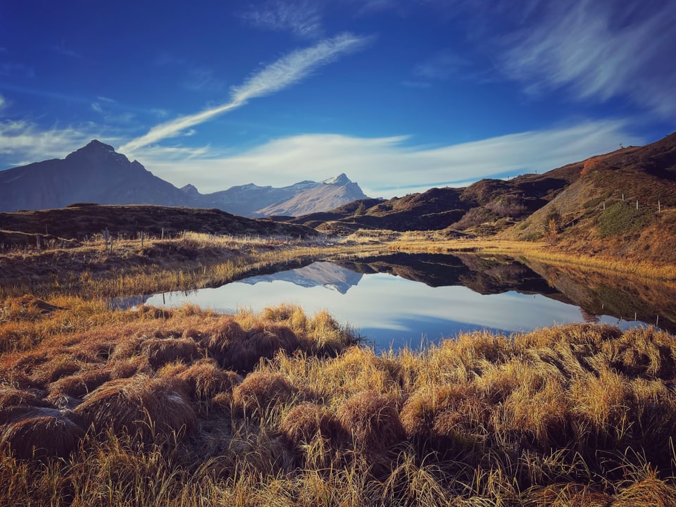 Bergsee mit Herbstlandschaft und Bergen im Hintergrund.