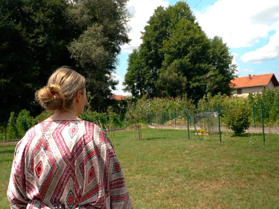 Frau steht draussen und schaut auf den Garten mit Bäumen.