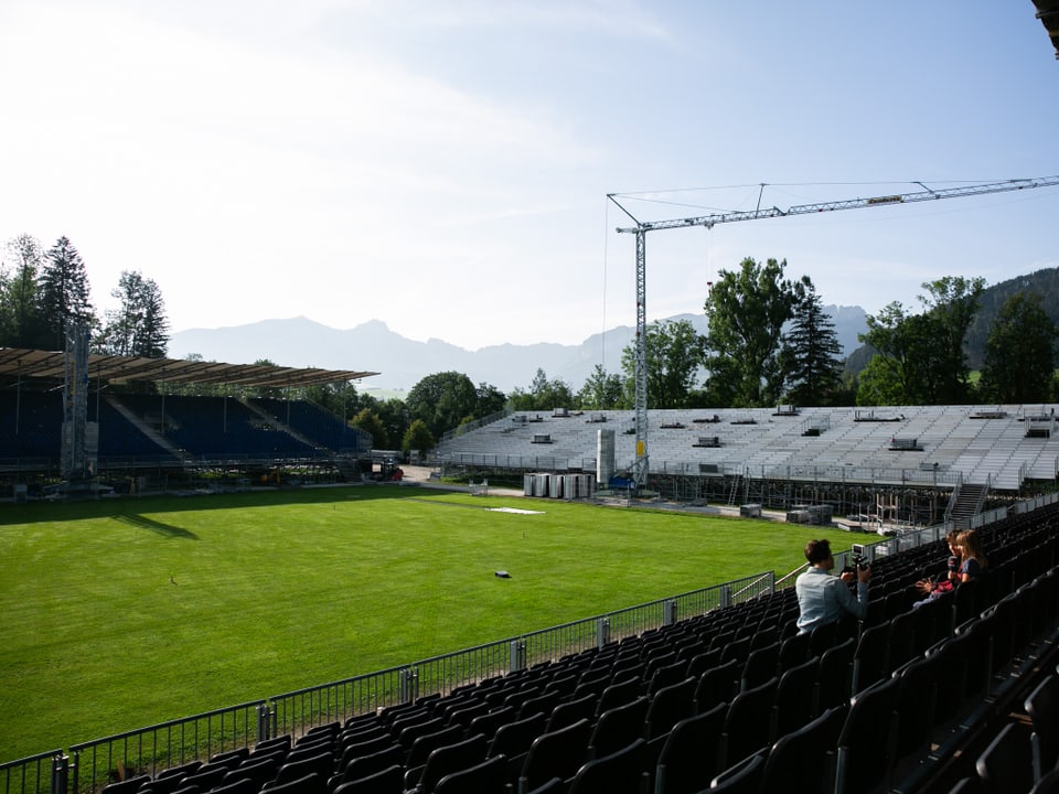 Ein Kran steht auf einem grünen Feld umgeben von Tribünen. 