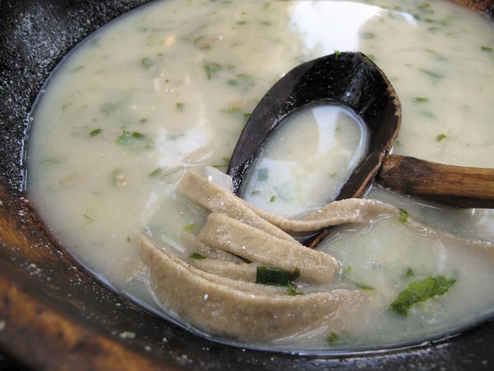 Nahaufnahme einer weisslichen Suppe, in der Kräter und Nudeln schwimmen.