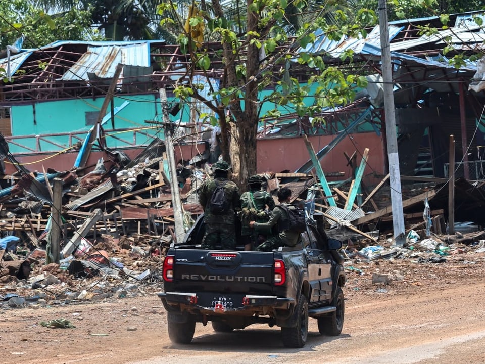 Soldaten in einem Pickup vor zerstörten Gebäuden