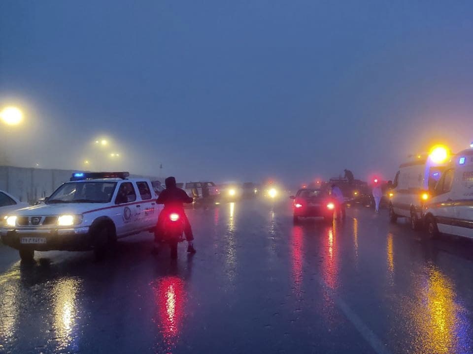 Nebeliger Abend, beleuchtete Autos und Polizeifahrzeuge auf nasser Strasse.