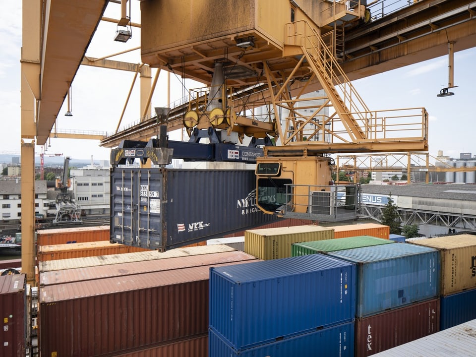 Ein riesiger, gelber Container-Kran hebt einen blauen Container auf.