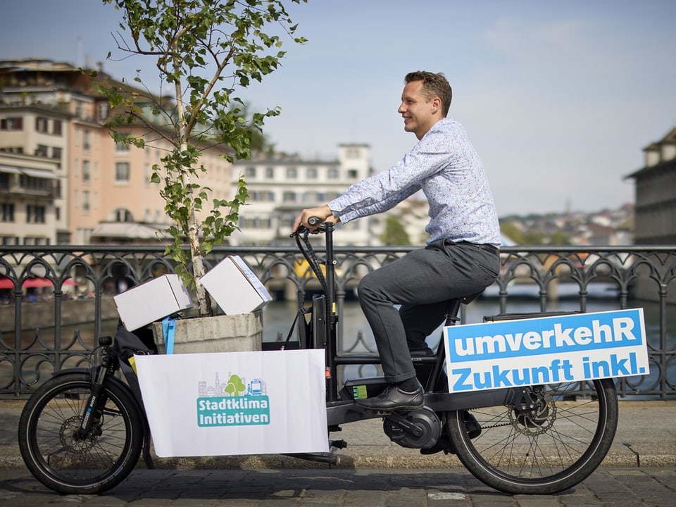 Mann fährt Lastenrad mit Banner 'umverkehr Zukunft inkl.' über Flussbrücke.