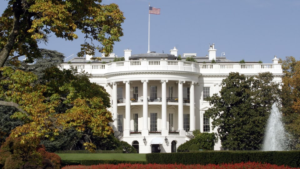 Weisse Haus mit amerikanischer Flagge und Garten.