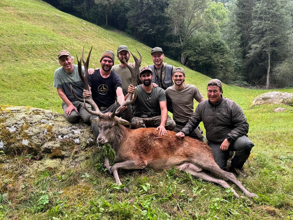 Gruppe Männer posiert mit erlegtem Hirsch im Wald.