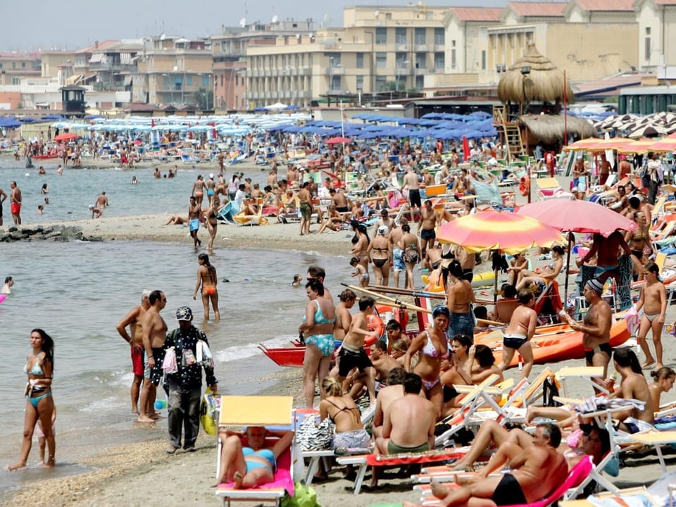 Überfüllter Strand mit vielen Menschen und Sonnenschirmen.