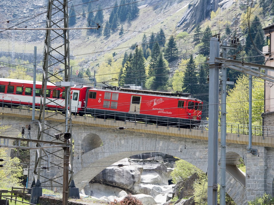 Eine rote Zugskomposition auf einer Brücke in den Bergen. 