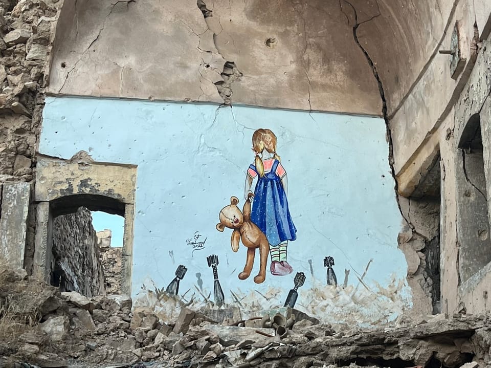Wandgemälde eines Mädchens mit Teddybär in zerstörtem Gebäude.
