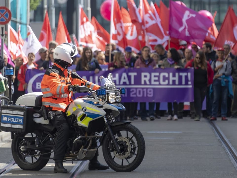 Demonstration, davor ein Polizist auf dem Motorrad.