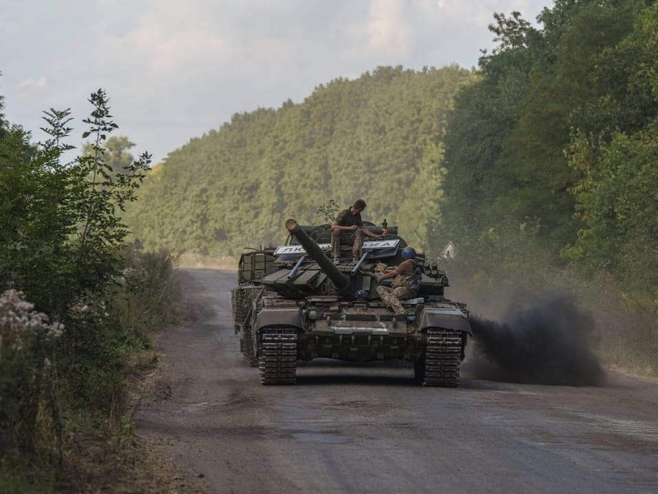 Panzer mit Soldaten auf schmaler Strasse mitten im Wald.