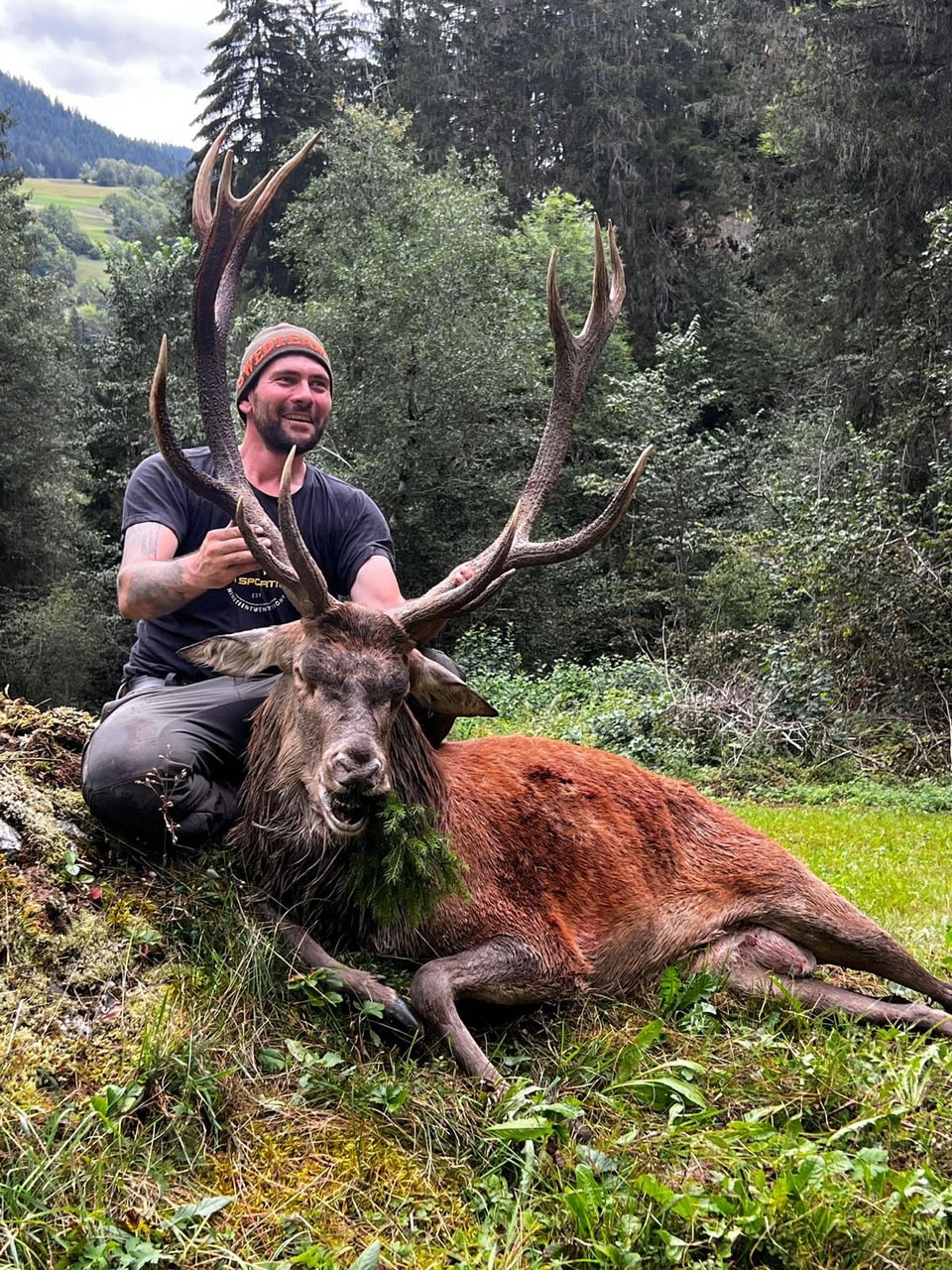 Jäger posiert mit erlegtem Hirsch im Wald.