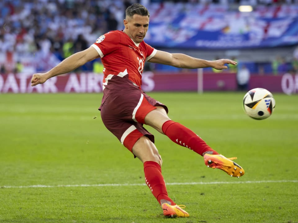 Fussballspieler im roten Trikot schiesst den Ball auf dem Spielfeld.