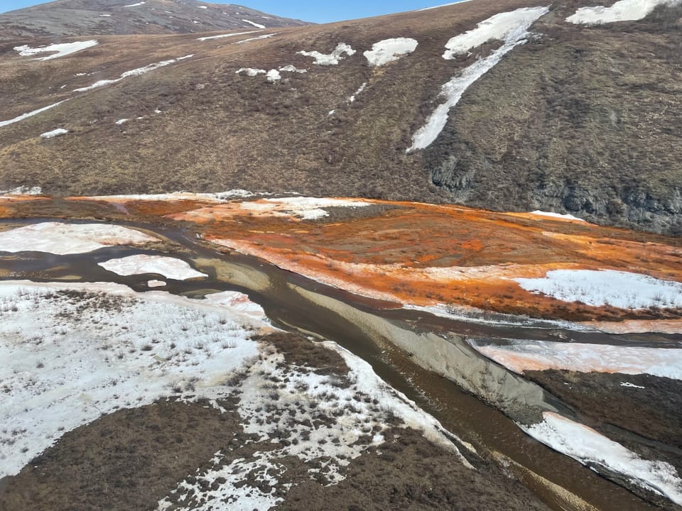 Schnee mit orange-Färbung an einem Fluss.