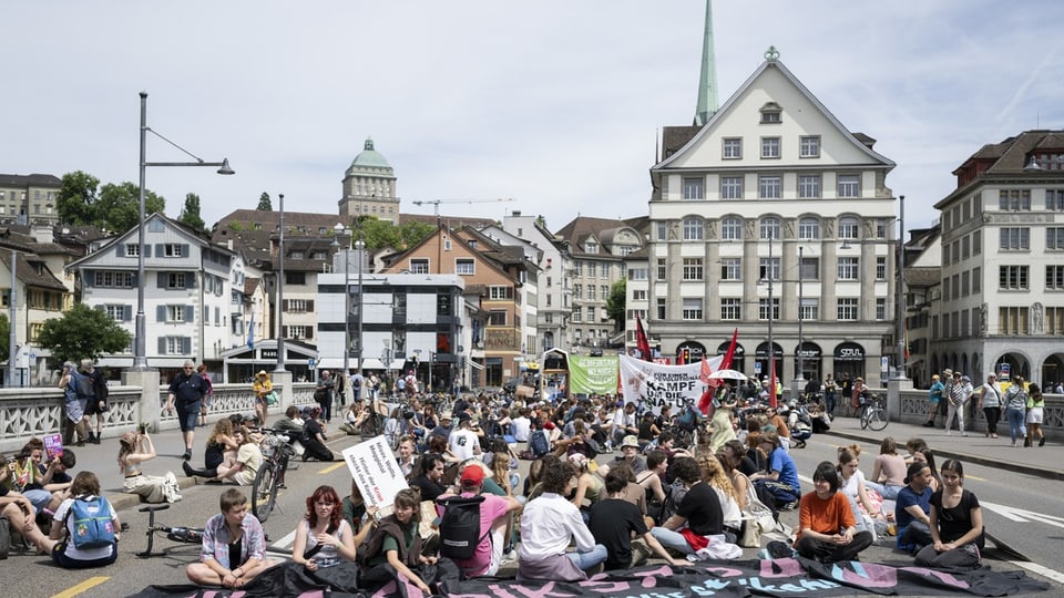 Menschen sitzen mit Protestschildern auf einer Brücke in der Stadt.