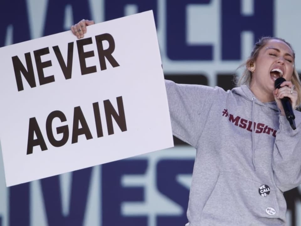 Miley mit Schild «Never Again» in der Hand