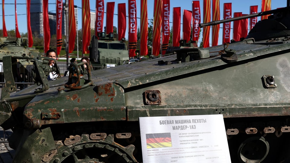 Ein rostiges gepanzertes Fahrzeug, davor ein Schild mit kyrillischer Schrift und einer deutschen Flagge.