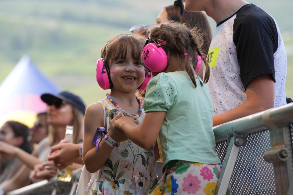 Zwei Mädchen mit Gehörschutz lachen bei einem Aussenkonzert.