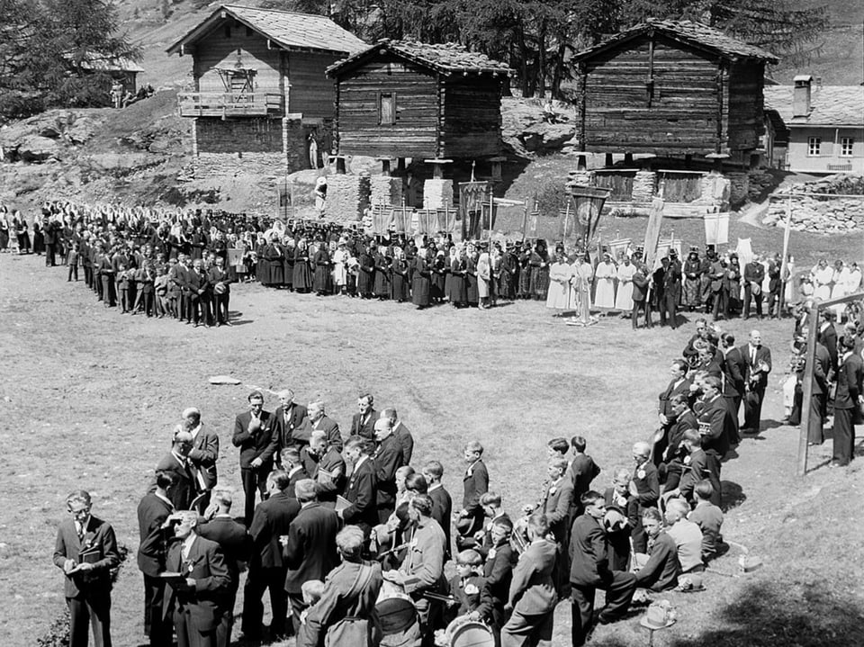 Menschenmenge bei einer Veranstaltung vor traditionellen Holzhäusern.