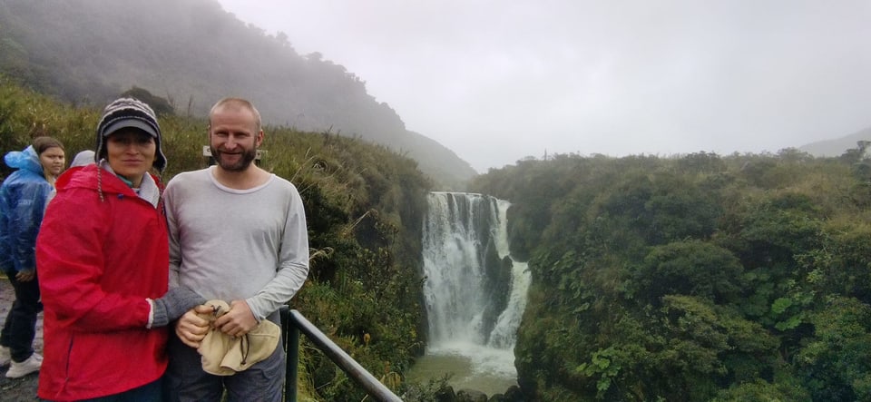 Menschen posieren vor einem Wasserfall in nebliger Landschaft.