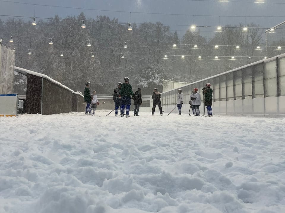 Menschen spielen bei Schnee auf einem beleuchteten Eisfeld.