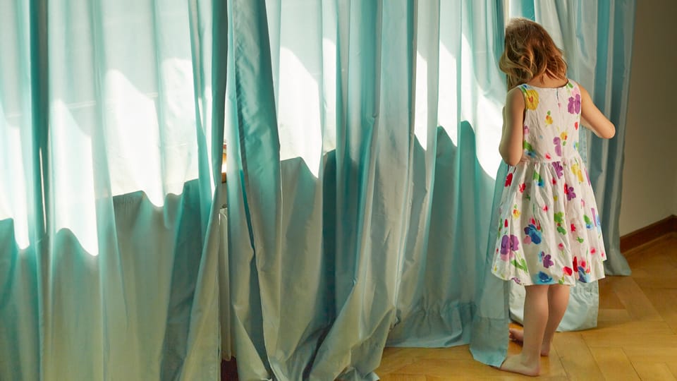 Ein kleines Mädchen in versteckt sich in einem Vorhang.