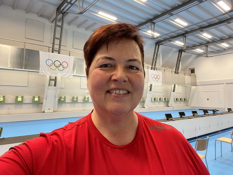 Heidi Diethelm steht in einer Schiesshalle mit Olympia-Flaggen.