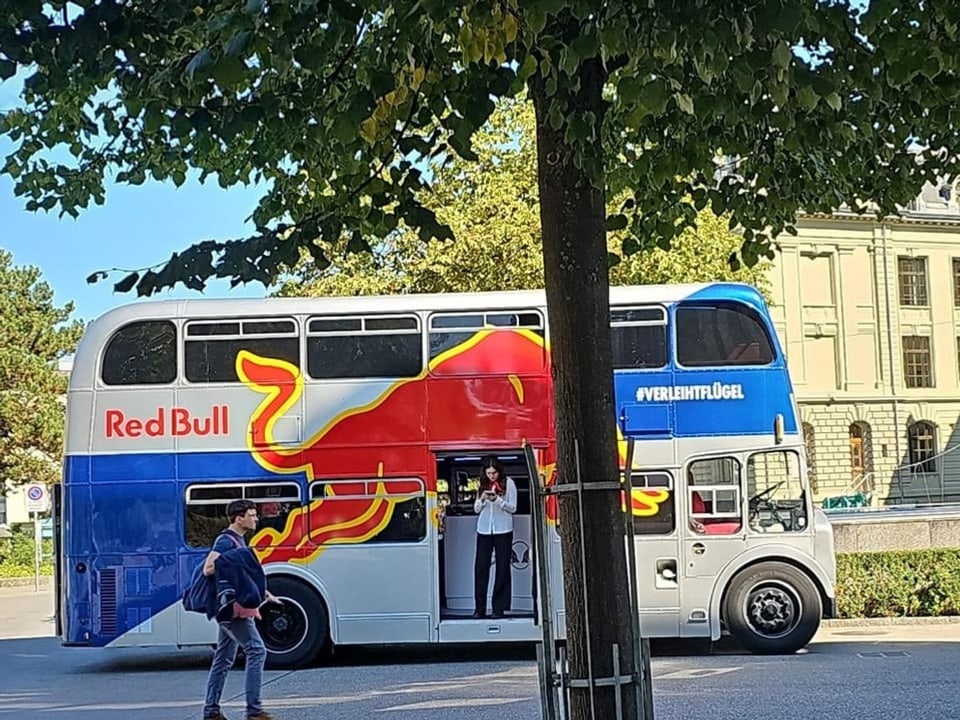 Ein Doppeldeckerbus von Red Bull vor einem Unigebäude.