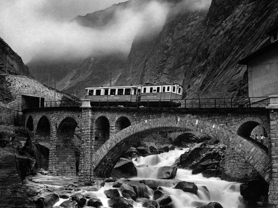 Historische Schwarzweiss-Aufnahme der Schöllenenschlucht mit Eisenbahnbrücke und Bahnwagen. 