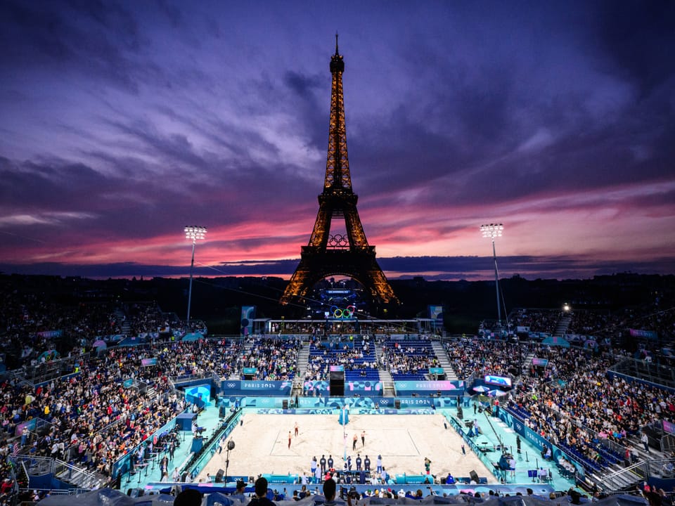 Volleyballspiel vor beleuchtetem Eiffelturm bei Sonnenuntergang.