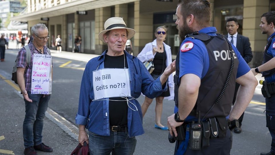 Demonstranten und ein Polizist stehen auf der Strasse. Ein Mann hat ein Schild umgehängt: "He Bill, geits no?!?"