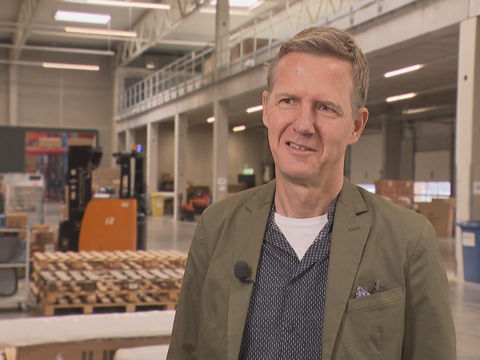 Mann in Lagerhalle, Paletten im Hintergrund.