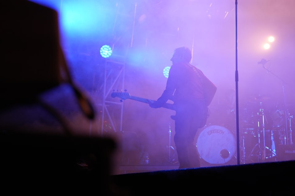 Musiker mit E-Gitarre auf Bühne in blauem und violettem Licht.