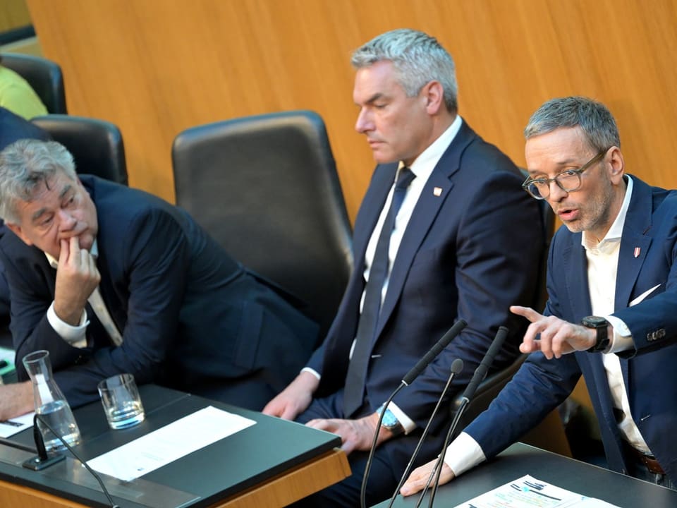 Kogler, Nehammer und Kickl sitzen an einem Tisch im Parlament, Kickl spricht in ein Mikrofon.