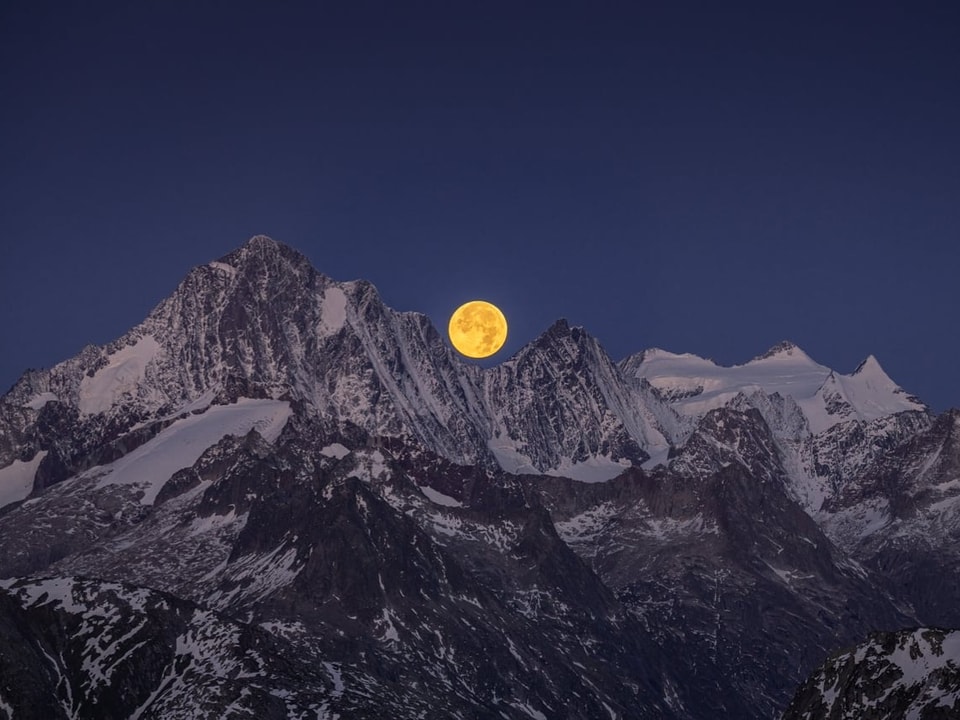 Vollmond über schneebedeckten Berggipfeln.