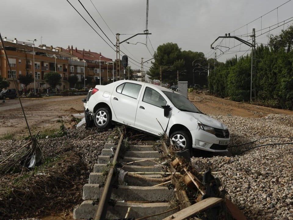 Weisses Auto auf beschädigten Bahngleisen in einer städtischen Umgebung.