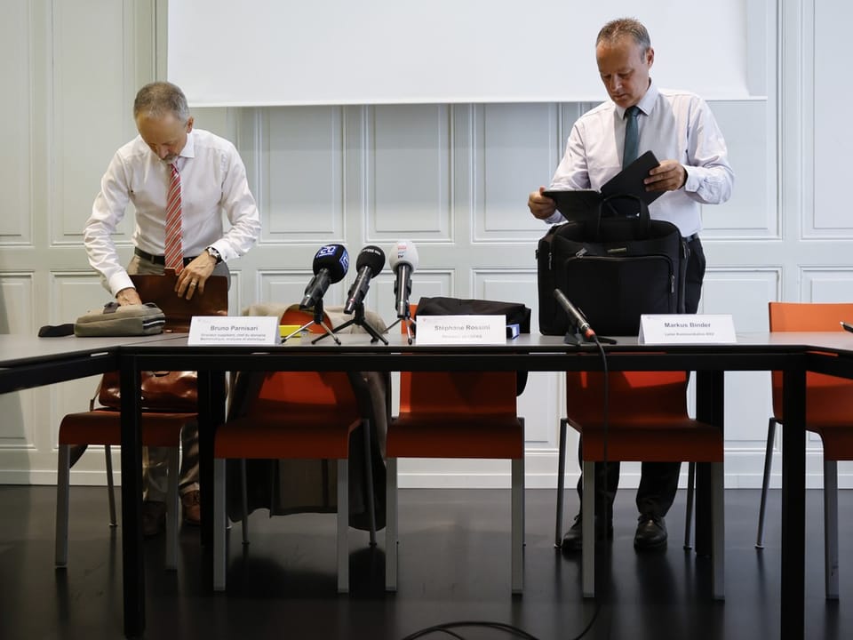 Zwei Männer packen ihre Taschen bei einem Pressetisch.