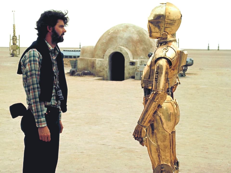 George Lucas steht neben dem Protokolldroiden C-3PO.