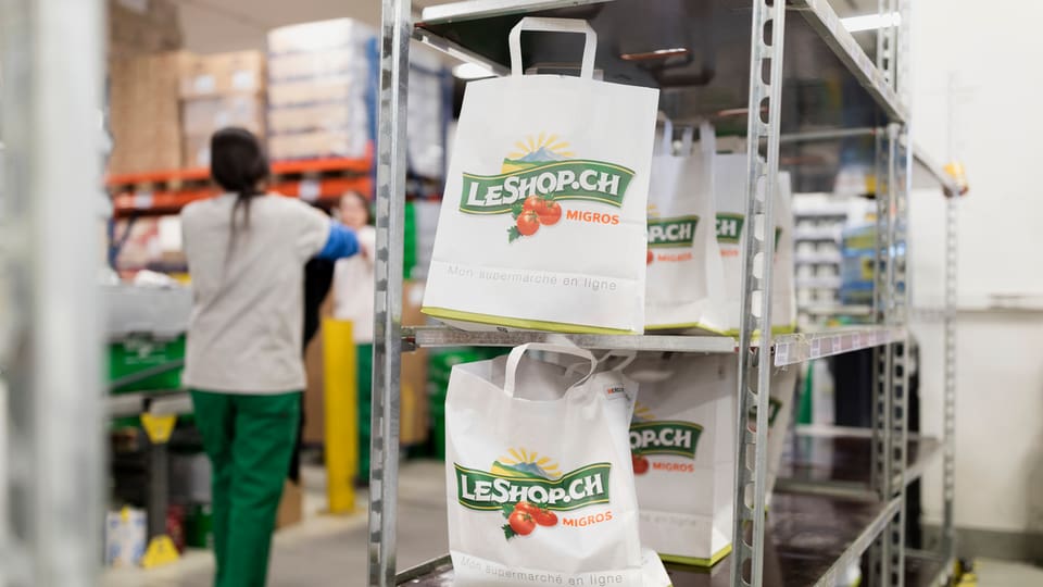 Einkaufstüten mit dem Le-Shop-Logo stehen in einem Regal.