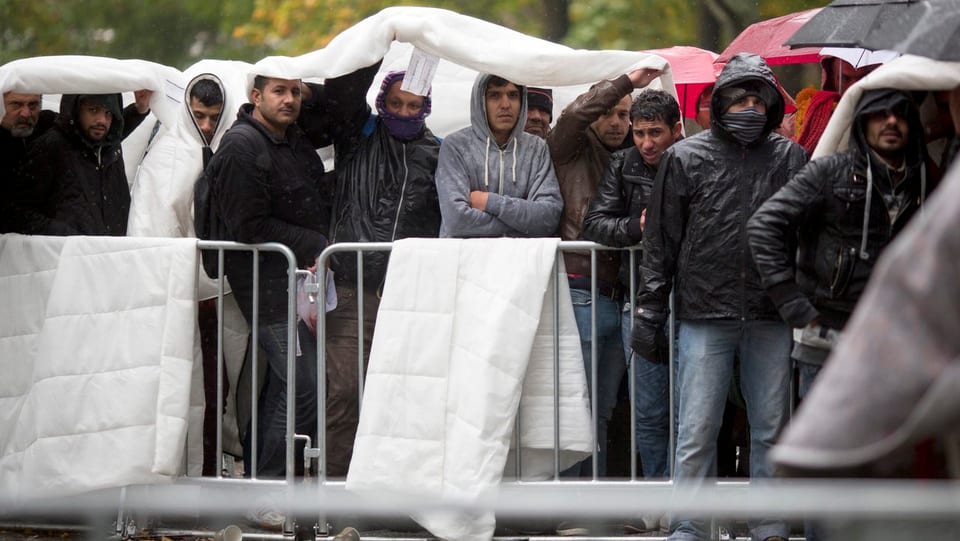 Flüchtlinge eine Schlange stehend und unter einer Plane.