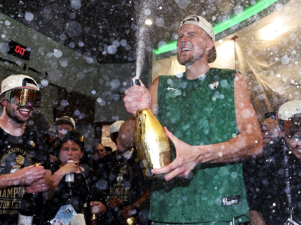 Feiernde Basketballspieler sprühen Champagner in einer Umkleidekabine.