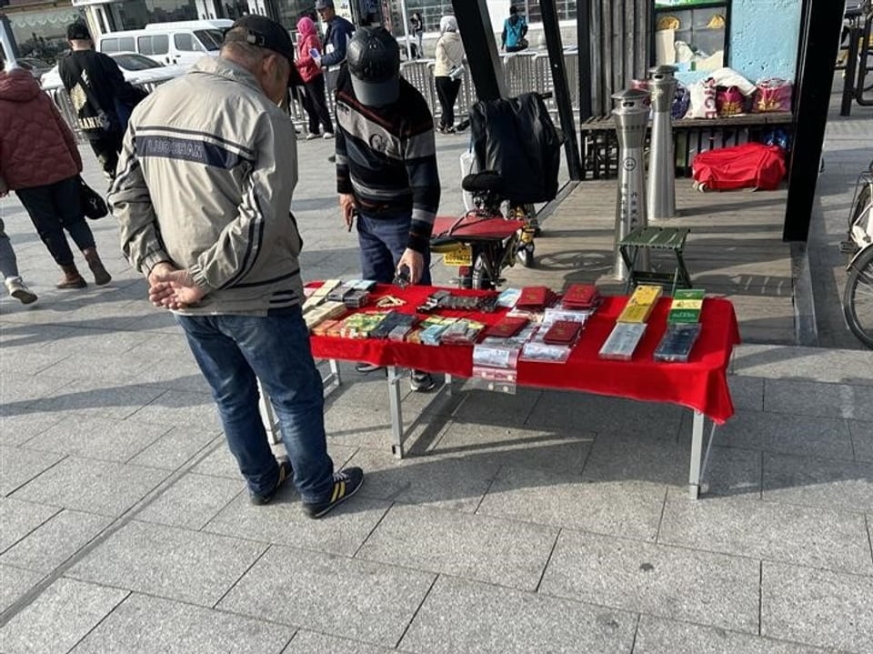 Zwei Männer betrachten einen Tisch mit Waren auf einem Gehweg.