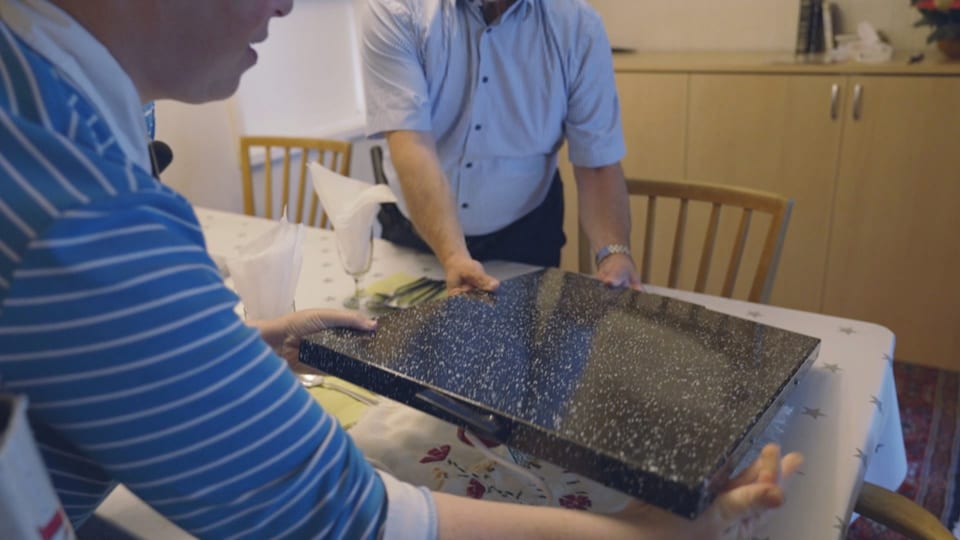 Zwei Personen halten eine schwarze Granitplatte über einem Tisch.