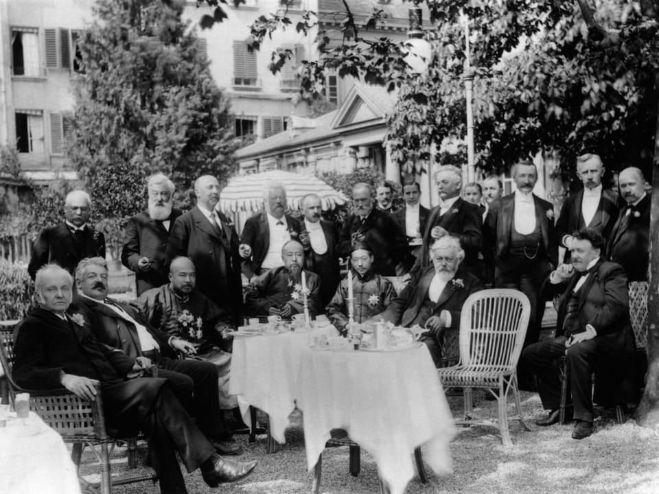 Gruppe von Männern in formeller Kleidung bei einem Gartenfest.