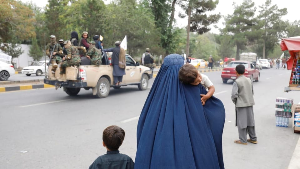 afghanische Frau mit zwei Kindern, im Hintergrund Taliban