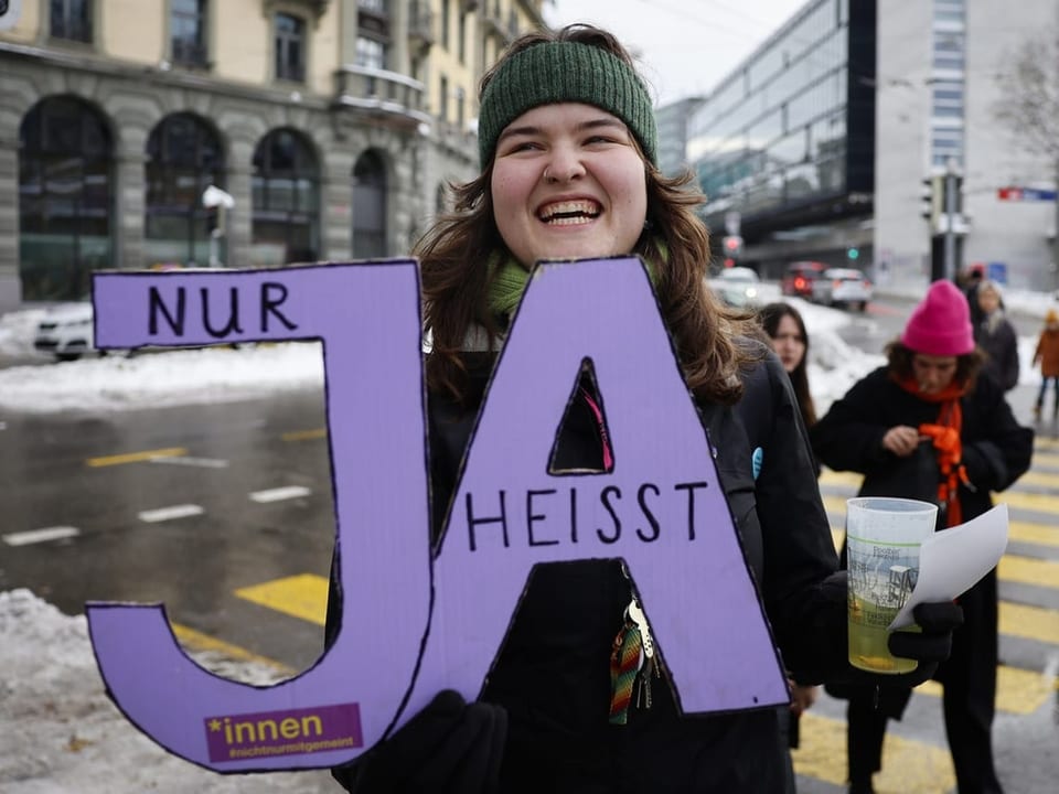 Frau hält 'Nur Ja heisst Ja'-Schild auf verschneiter Strasse.