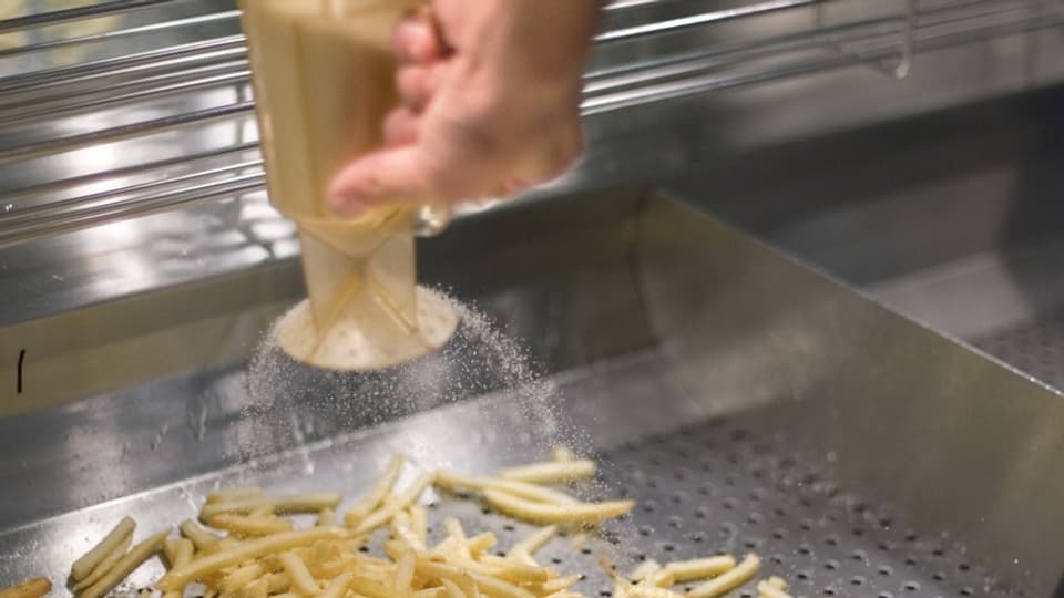Hand streut Salz auf Pommes Frites.