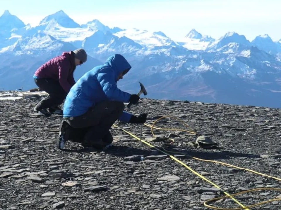 Zwei Forschende befestigen auf einem Bergplateau Sensoren mit einem Hammer.