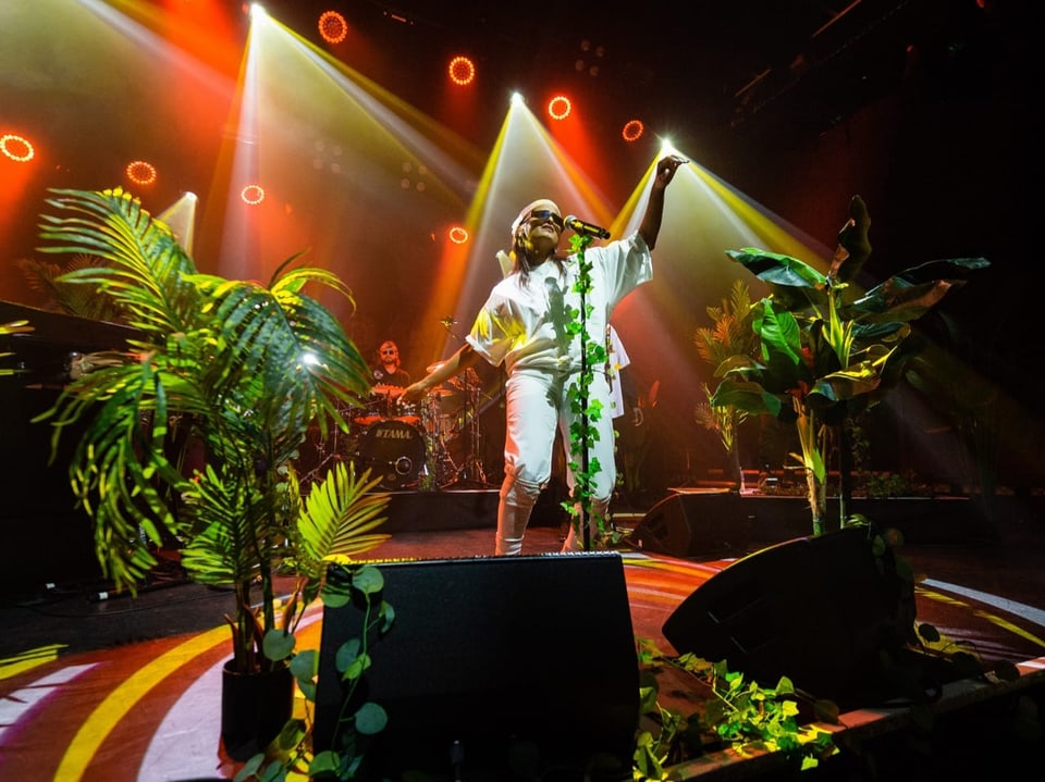 Sängerin performt auf Bühne mit Pflanzen und bunten Lichtern.